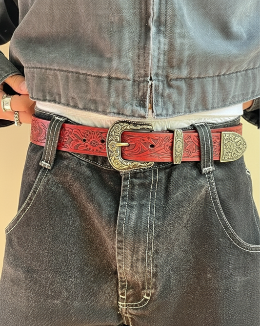 Person wearing a red belt with a decorative buckle on dark jeans.