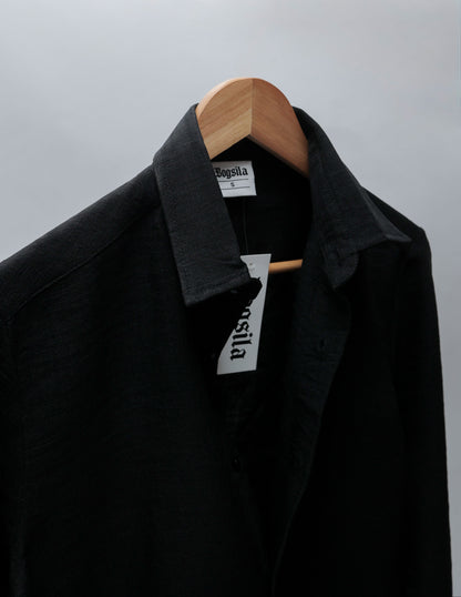 A black collared shirt jacket from the brand Bogula, hanging on a wooden hanger against a light gray background.