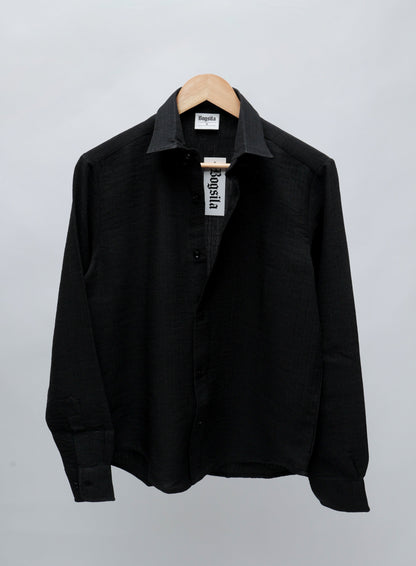 A black long-sleeve button-up shirt with a pointed collar, hanging on a wooden hanger against a light gray background.