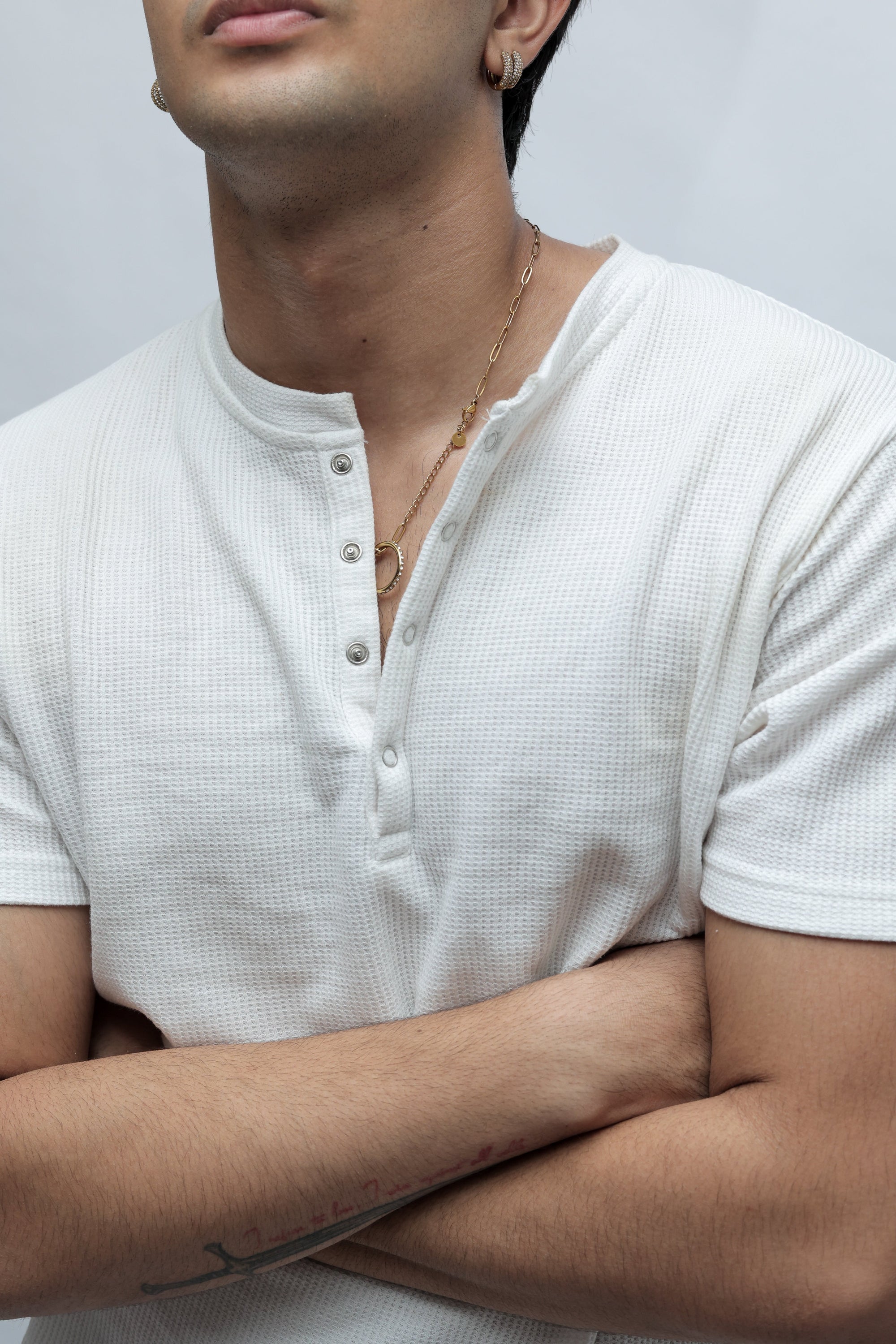 A close-up lifestyle shot of a man wearing a white waffle-knit short-sleeve henley shirt, showing the texture of the fabric and the snap-button placket.