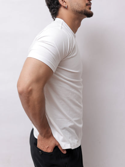 A man in a white t-shirt and black pants performing a push-up against a plain light gray background.