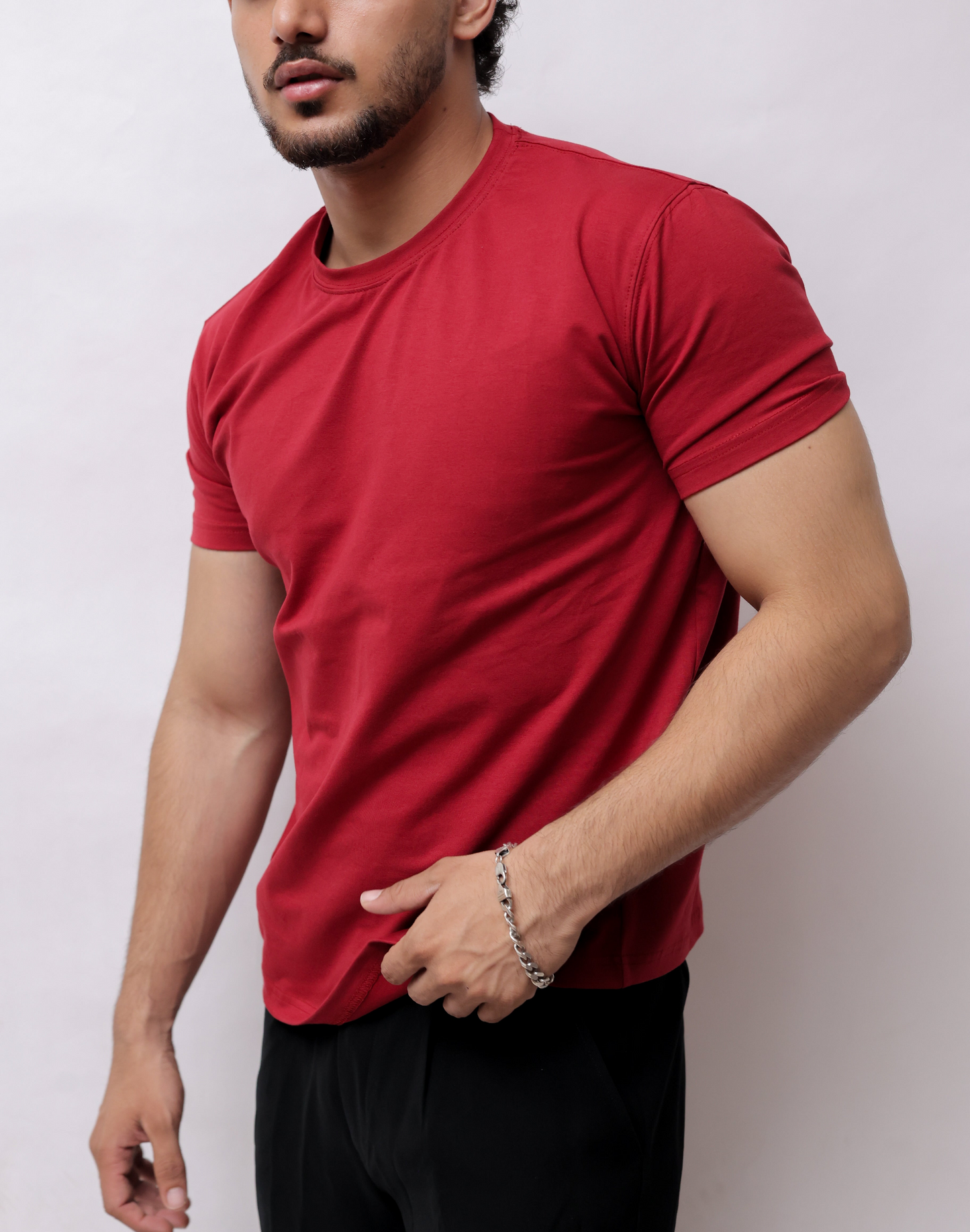 A man wearing a red short-sleeve crewneck t-shirt and black pants, shown from a side profile against a plain light gray background.
