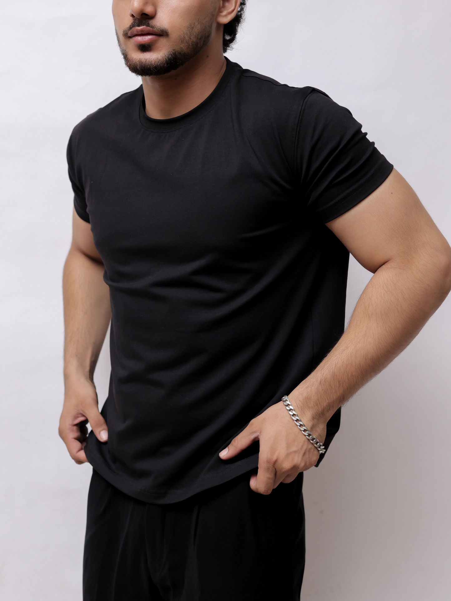 A man wearing a black short-sleeve t-shirt and black pants, shown from a side angle against a plain light gray background.