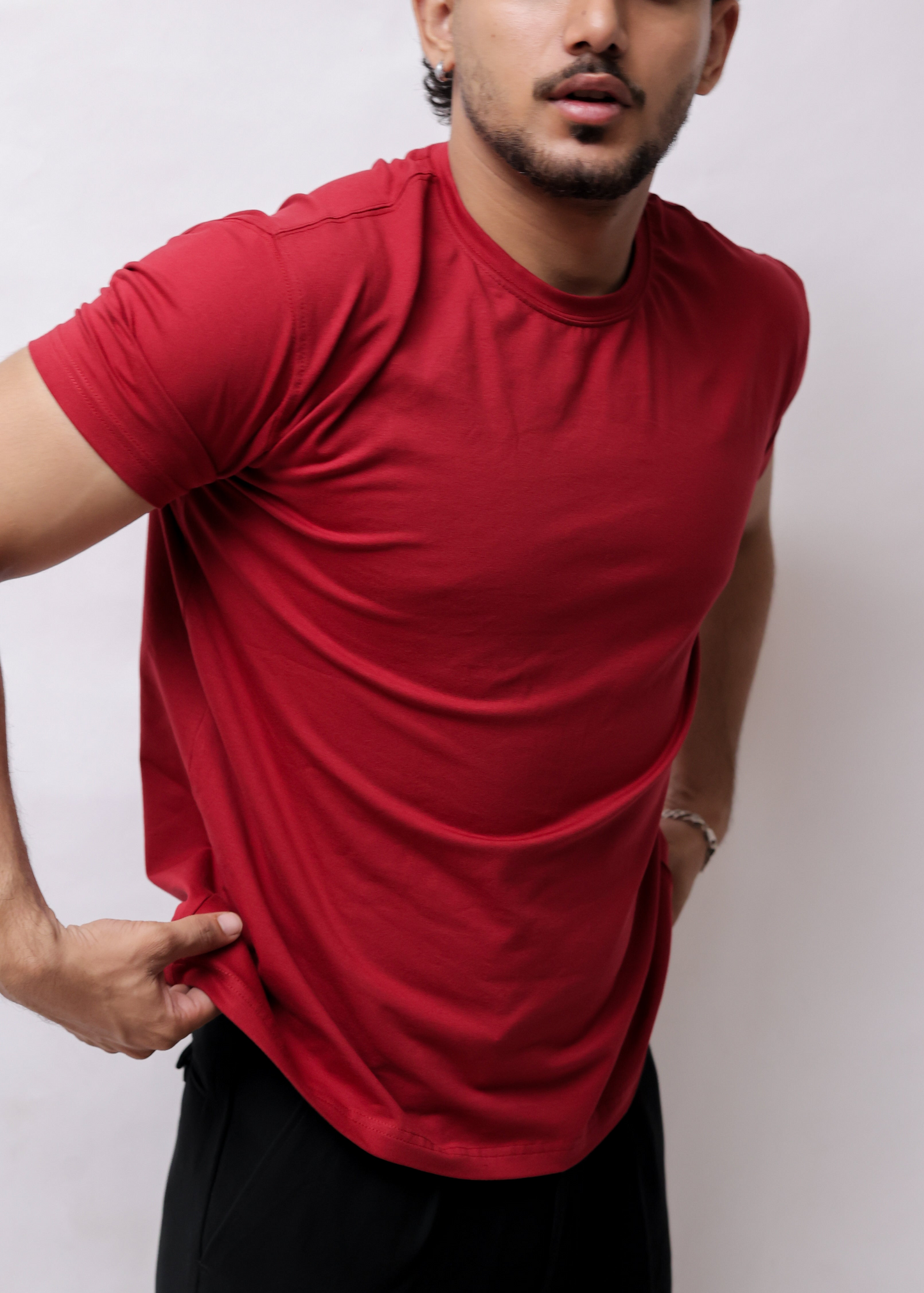 A man wearing a red short-sleeve athletic t-shirt and black pants, shown from a high-angle side view against a plain light background.