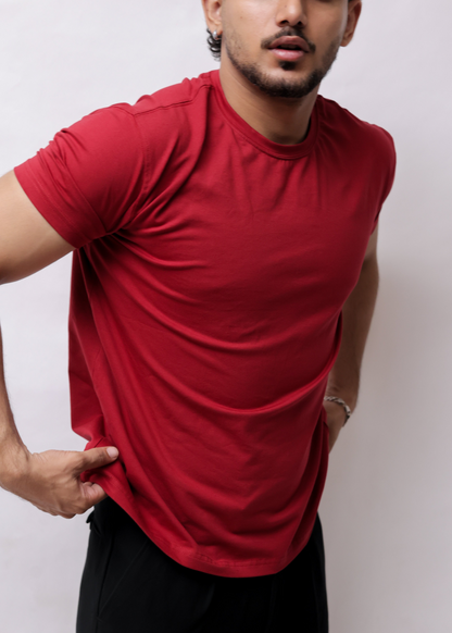 A man wearing a red short-sleeve athletic t-shirt and black pants, shown from a high-angle side view against a plain light background.