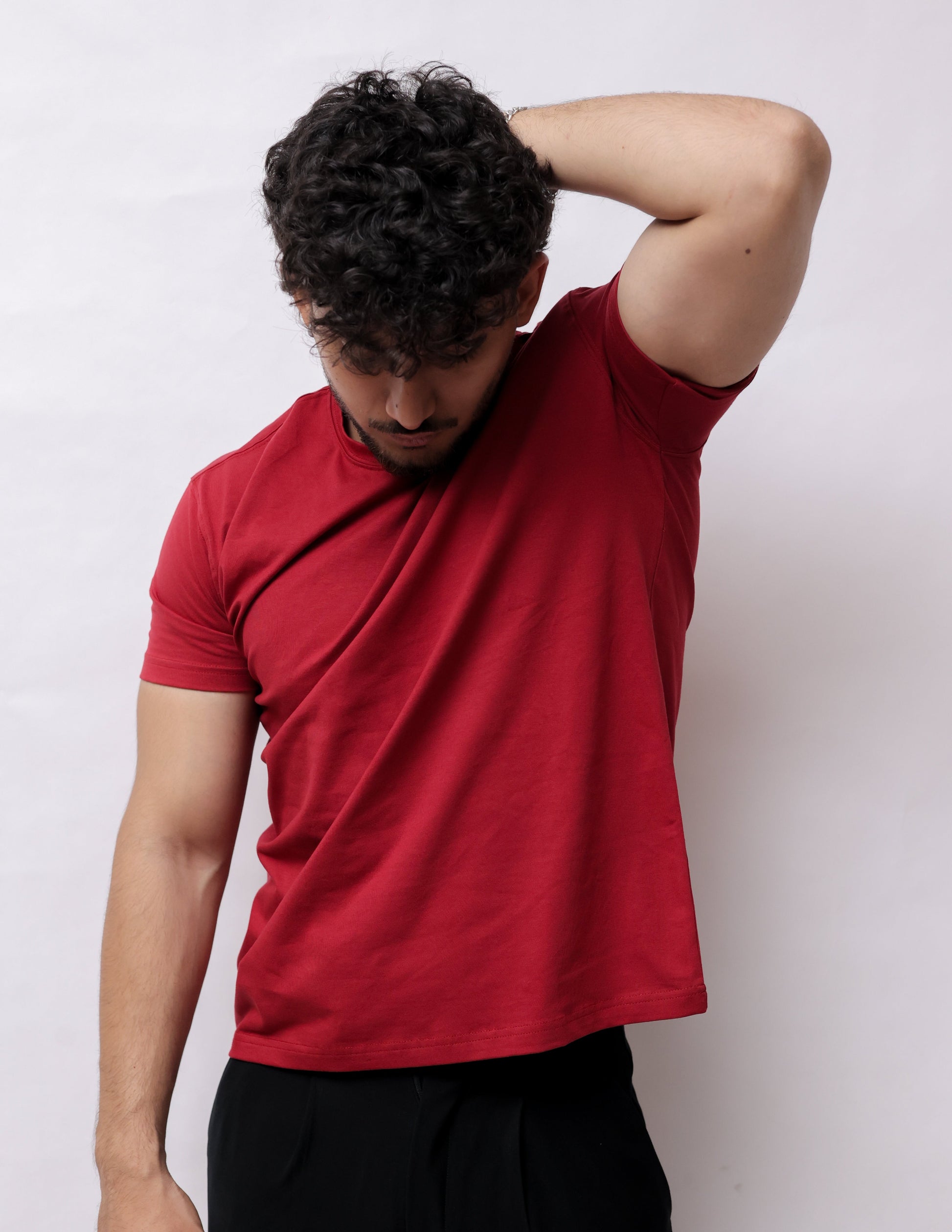 A man wearing a red short-sleeve t-shirt and black pants, lying on his side against a plain white background.